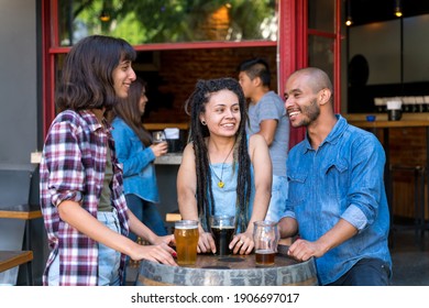 A Group Of Friends Standing Outdoor At A Brewery Barrel While Having Drinks And Fun Talking.