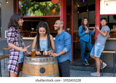 A Group Of Friends Standing Outdoor At A Brewery Barrel While Having Drinks And Fun Talking.