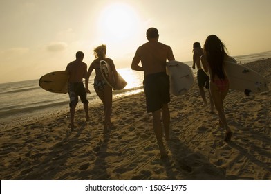 Group of friends with surfboards running towards ocean at sunset - Powered by Shutterstock