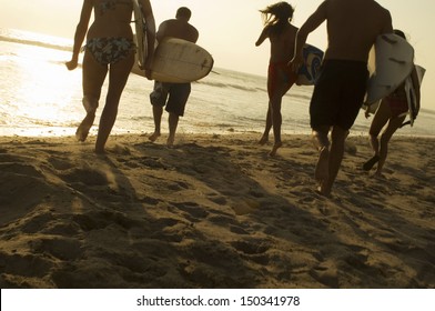 Group of friends with surfboards running towards ocean at sunset - Powered by Shutterstock