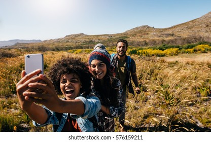 Group of friends taking selfie on country hike. Young people hiking in countryside and taking pictures with smart phone.