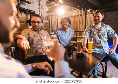 Group of friends talking and drinking beer while sitting in pub. Multicultural group. - Shutterstock ID 1225917988