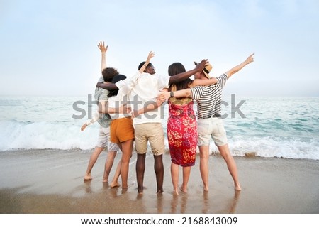 A group of friends with their backs to the camera enjoying the sea together - Multicultural multinational happy people hugging into the sun carefree and happiness, vacation on sea.