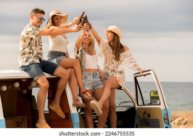 Group of friends toasting with beer sitting in the top of a camper van parked on a beach - Powered by Shutterstock