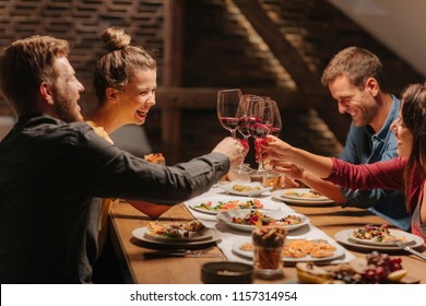 Group of friends toasting with wine glasses at home celebration and laughing.