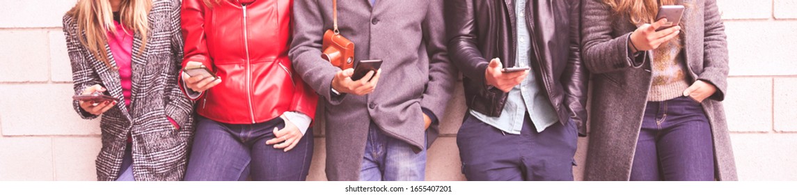 Group of friends using apps on their mobiles. Hipsters addicted to technology. Concept of youth, social and friendship. Group of multiracial friends watching smart mobile phones and taking selfies.
