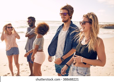 Group Of Friends Walking Along A Beach At Summertime. Happy Young People Enjoying A Day At Beach.