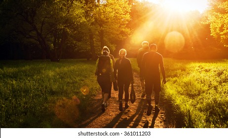 Group of friends walking with backpacks in sunset from back. Adventure, travel, tourism, hike and people friendship concept. Sports activity