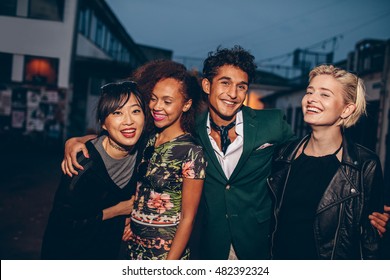 Group Of Friends Walking On City Street Together At Night. Multiracial Young Man And Women Enjoying Outdoors In Evening.