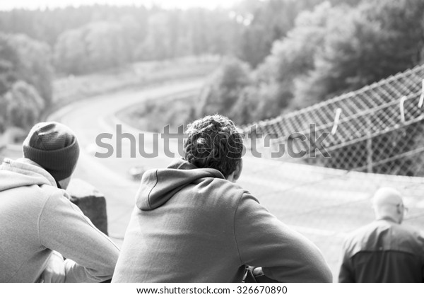 A group of friends watching\
a car race on a legendary racing track in Germany. People are\
watching the race behind a metal fence. Image has a vintage effect\
applied.