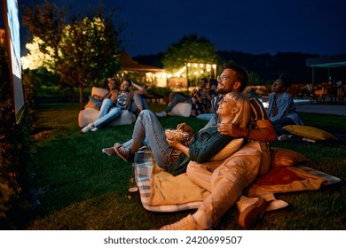 Group of friends watching a movie in the evening in the backyard. Focus is on couple eating popcorn.  - Powered by Shutterstock