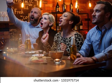 Group Of Friends Watching Tv In A Cafe Behind Bar Counter