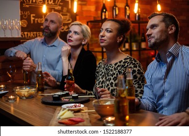 Group Of Friends Watching Tv In A Cafe Behind Bar Counter