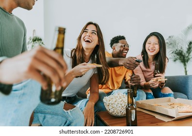 Group of friends watching tv and eating pizza - Multiracial cheerful young people having weekend home party together - Happy students having fun in university rooms - Youth lifestyle and food concept - Powered by Shutterstock