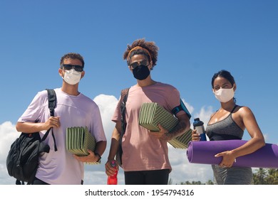 Group of friends wearing masks dressed in sportswear holding sports equipment ready to train on the beach. - Powered by Shutterstock