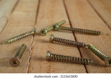 A group of gilded self-tapping screws randomly scattered on a wooden surface. Space for text.