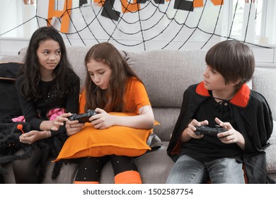 Group Of Girl And Boy Kids Smiling And Dress Up As Halloween Vampire Costume Holding Joystick To Play Halloween Game In Living Room At Home Together