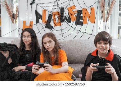 Group Of Girl And Boy Kids Smiling And Dress Up As Halloween Vampire Costume Holding Joystick To Play Halloween Game In Living Room At Home Together