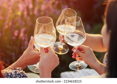A group of girlfriends raise a toast with glasses of white colored wine on a sunset. Close shot.
