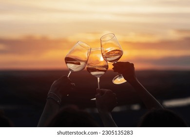 A group of girlfriends raise a toast with glasses of white wine on a sunset. Close shot.	 - Powered by Shutterstock