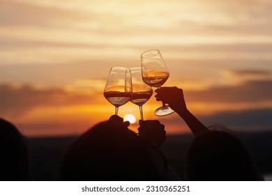 A group of girlfriends raise a toast with glasses of white wine on a sunset. Close shot.	
