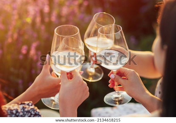 A group of girlfriends\
raise a toast with glasses of white colored wine on a sunset. Close\
shot.