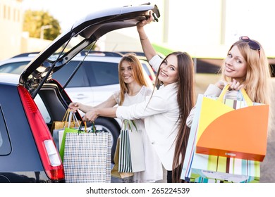 Group Of Girls After Shopping Loading A Shopping Bags In A Car Trunk