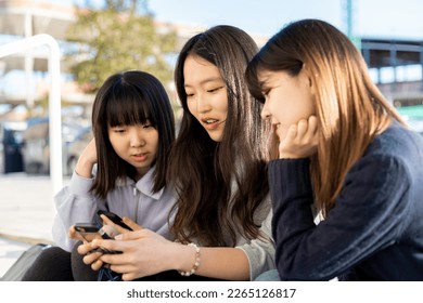 Group of girls with Asian features sitting on the steps of a street, The girl in the middle has the mobile while the girls outside watch. Concept of searching for information on mobiles,social networ