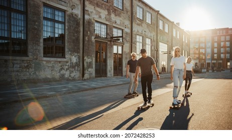 Group of Girls and Boys on Skateboards Through Fashionable Hipster District. Beautiful Young People Skateboarding Through Modern Stylish City Street During Golden Hour. - Powered by Shutterstock