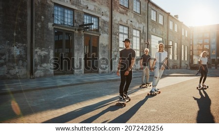 Group of Girls and Boys on Skateboards Through Fashionable Hipster District. Beautiful Young People Skateboarding Through Modern Stylish City Street During Golden Hour.