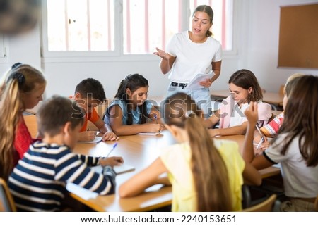 Group of girls and boys studying in school, sitting around desks and attending teacher's lecture.