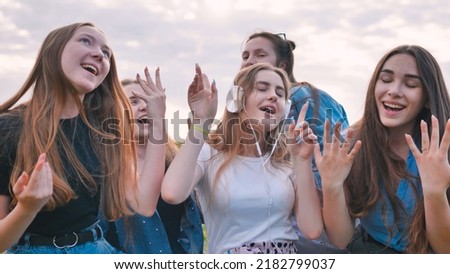 A group of girls of friends are listening to music on headphones and dancing to a friend.