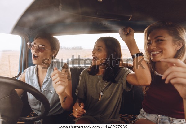 Group of girls having\
fun in the car. Women friends singing songs and dancing in car\
during road trip.