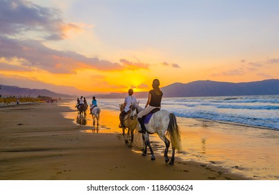 A group of girls on horseback riding on a sandy beach on the background of the sunset sky - Powered by Shutterstock