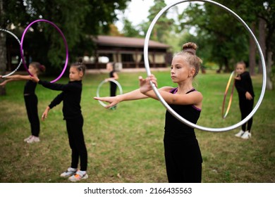 Group Of Girls Trainees Doing Exercise With Hoop On Rhythmic Gymnastics Training Outdoors In Sports Camp In Summer