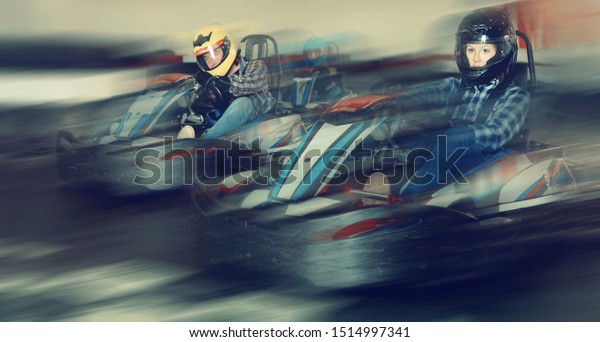 Group of glad  smiling people driving go-carts at
racing track