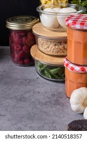 Group Of Glass Piled And Covered Containers Full Of Homemade Meal Over A Cement-like Gray Table.