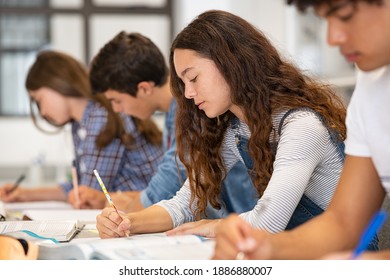 Group of guys and girls doing class assignment in the library. Young university students reading books for study. Group of high school students studying for exam in classroom sitting in a row.