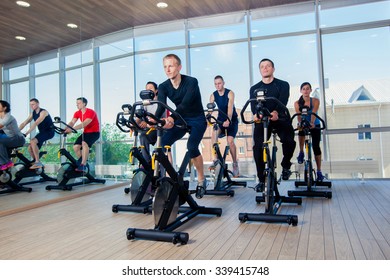 Group Of Gym People On Machines, Cycling In Class.