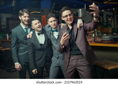 Group Of Handsome Young Men Dressed In Elegant Classic Suits Relax In A Bar And Take A Selfie. Men's Fashion. Business People Club.