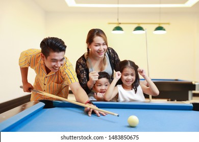 Group Of Happiness Asian Family Father, Mother, Son And Daughter Playing Billiard Or Snooker On Blue Pool Table With Happy Smiling Face During Holiday Vacation