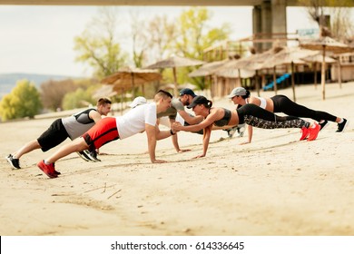 Group Happiness Young Friends Having Workout On The Beach. They Are Doing Plank Exercise Together.