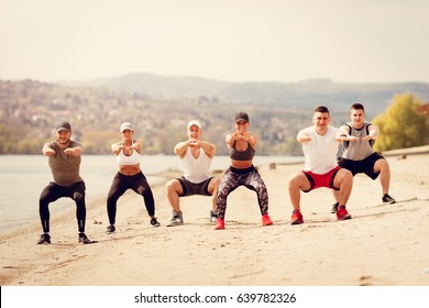 Group happiness young friends having workout together on the beach. They are doing squats exercise.