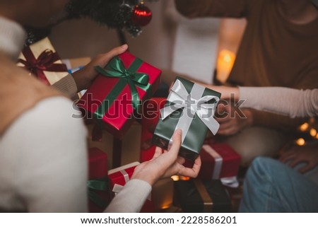 Group of happy Asian friends celebrating Christmas and decorate the Christmas tree indoors. Beauty woman with Christmas Gifts. New Year party. Woman hands decorate Christmas tree red ball, bauble.