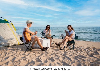 Group of happy Asian friends playing guitar and singing with clap while picnic and camping on the beach in outdoors vacation summer. Young male, female tourist smile fun at party near tent on seaside. - Powered by Shutterstock