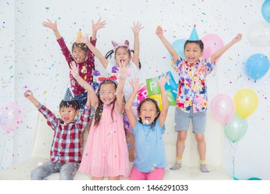 Group Of Happy Asian Kids Raise Hands Up And Enjoy Throwing Colorful Confetti With Friends In Birthday Party