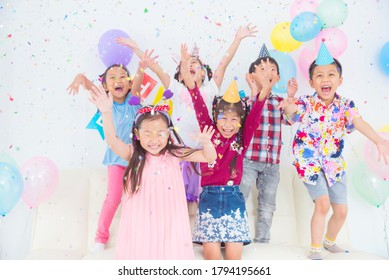 Group Of Happy Asian Kids Raise Hands Up And Enjoy Throwing Colorful Confetti With Friends In Birthday Party.