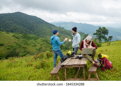 Group Of Happy Asian Man And Woman Friends Backpacker Enjoy Hiking And Drinking Coffee Together On Forest Mountain In Autumn. Young Woman Using Laptop Computer Online Working In Outdoor Vacation
