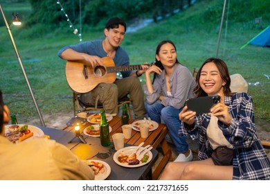 Group Of Happy Asian Man And Woman Friends Enjoy And Fun Outdoor Lifestyle Using Mobile Phone Taking Selfie Or Video Call Together While Hiking And Camping On Holiday Travel Vacation At Summer Night.