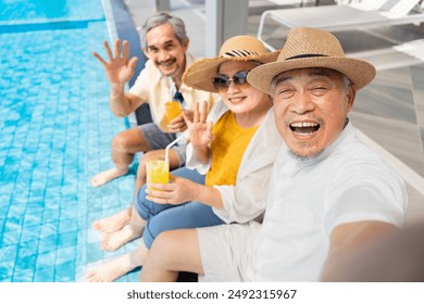 group of happy asian senior friends taking selfie while sitting,drinking and relaxing at poolside,elderly retired people enjoy summer trip at luxury resort and spa - Powered by Shutterstock